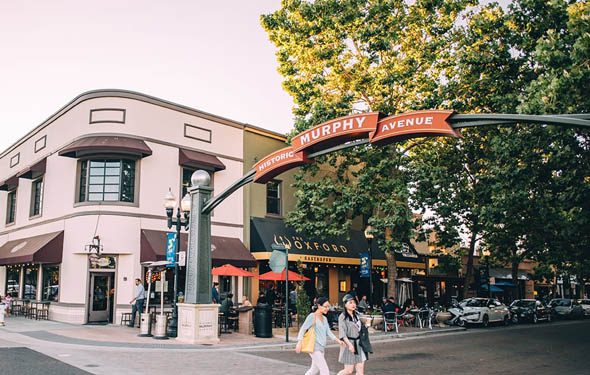 Historic Murphy Avenue with busy sidewalks, bright storefronts, tall trees, and people walking.